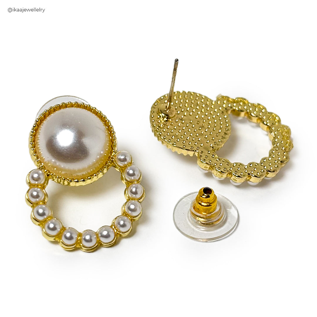 Close-up of delicate gold Riva Earrings with a hammered texture, resting on a white surface.