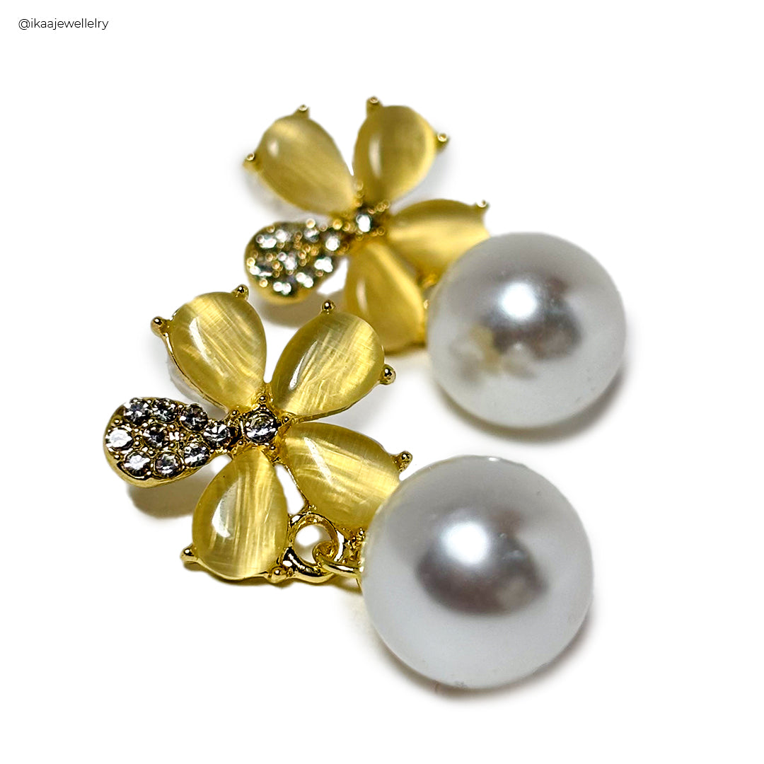 Gold Kia earrings with a small, delicate charm, displayed on a white background.