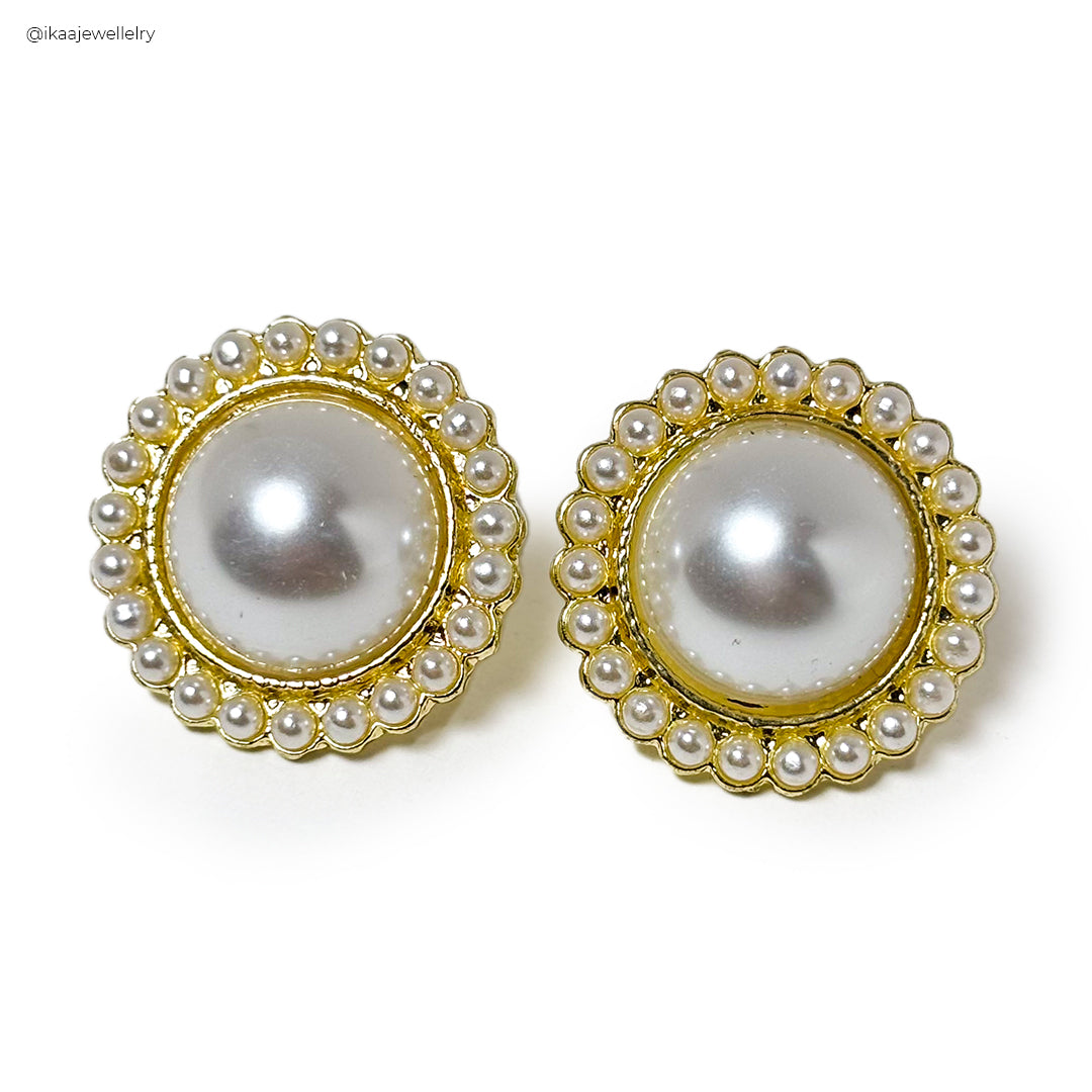 Close-up of Misha Earrings: delicate gold hoops with a dangling pearl, showcased against a soft grey background.