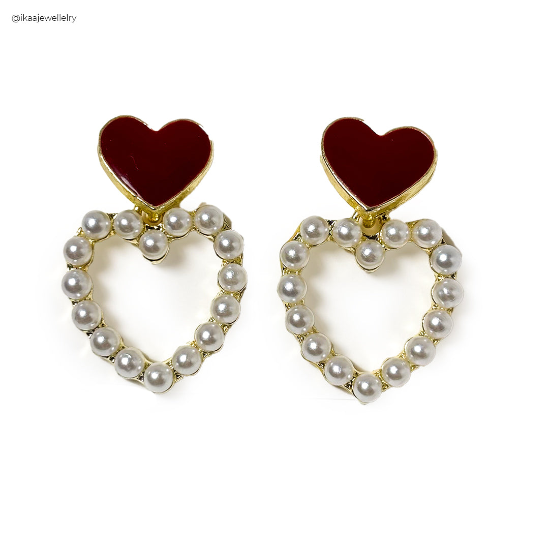 Premika Earrings: Close-up of delicate gold hoop earrings with a single pearl drop, resting on a white surface.